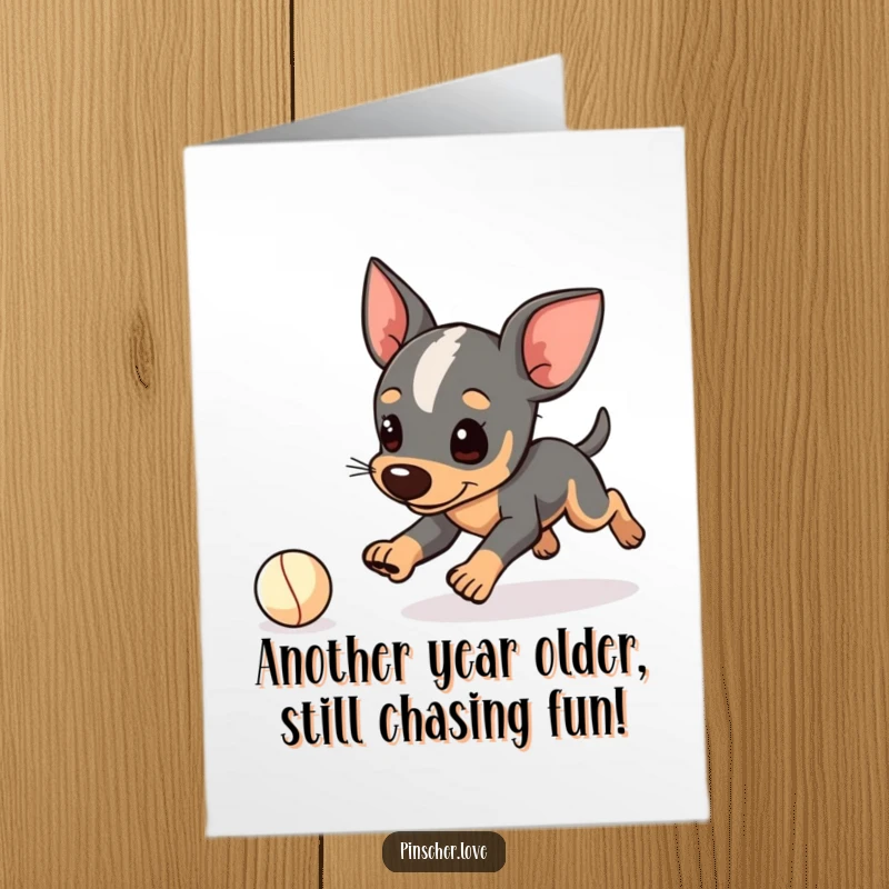 Funny Free Printable Birthday Card featuring a pinscher character playfully tripping while chasing a tiny ball, adding comic relief.