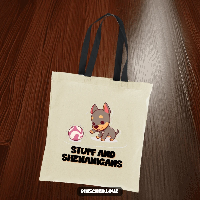 Funny Pinscher Tote Bag: A mischievous pinscher playfully nudges a bouncing, crinkly ball, showcasing adorable and energetic canine interaction.