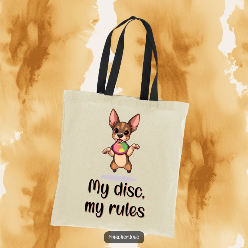Funny Pinscher tote bag illustrated with a determined dog preparing to leap for a vibrant, flying disc, capturing athletic excitement.